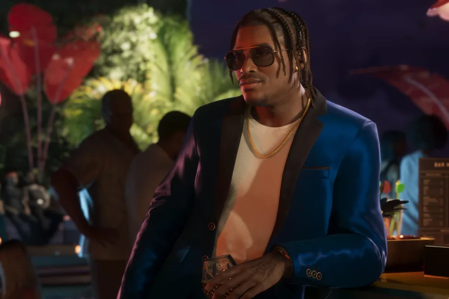 A man in an electric-blue suit with satin lapels, braided hair, sunglasses and a gold chain, holding a glass and leaning on the bar at an evening poolside party.