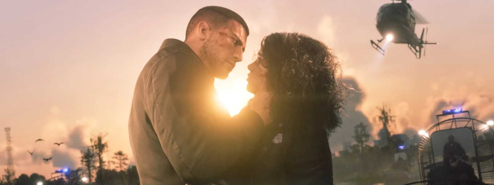 Two characters embracing face to face against the setting sun in the wetlands; a helicopter and police airboats with flashing lights surround them.