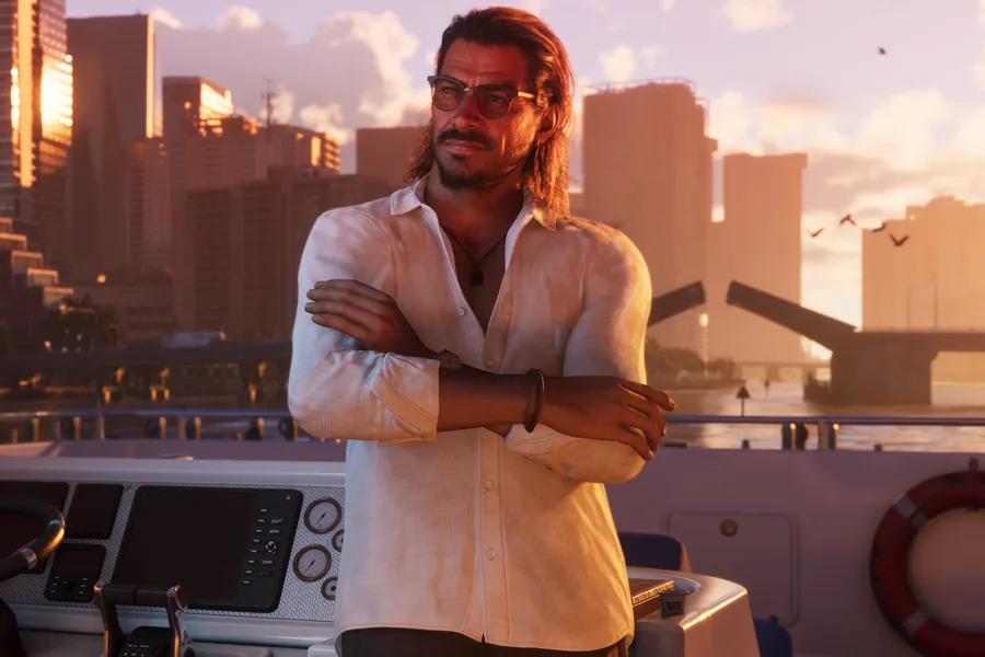 A man with long brown hair, sunglasses and an open white shirt stands with arms crossed at a boat's helm; skyscrapers and a raised drawbridge at sunset.