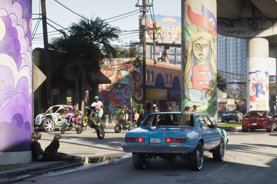 A Vice City street beneath an overpass whose pillars are covered in colourful murals: a blue sedan in profile, motorbikes and a quad popping a wheelie, painted storefronts and palm trees.